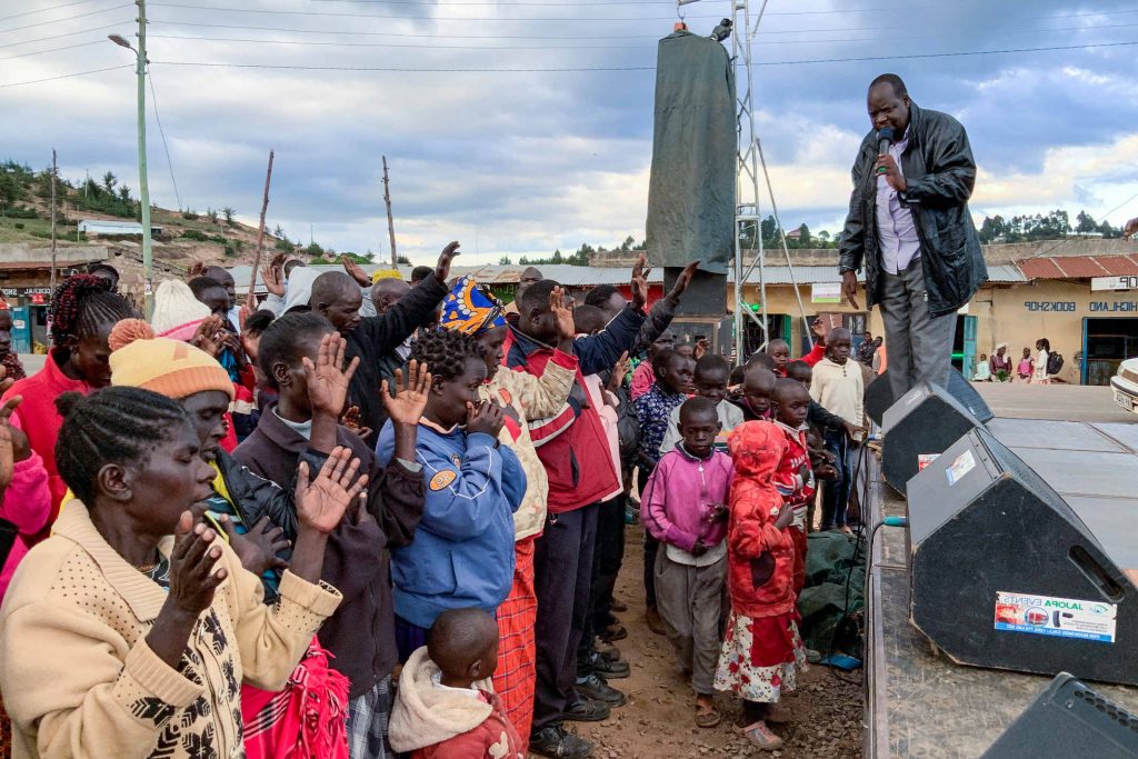 A Christian Evangelist in Kenya preaches the gospel to a group of Kenyans while standing outside on a stage