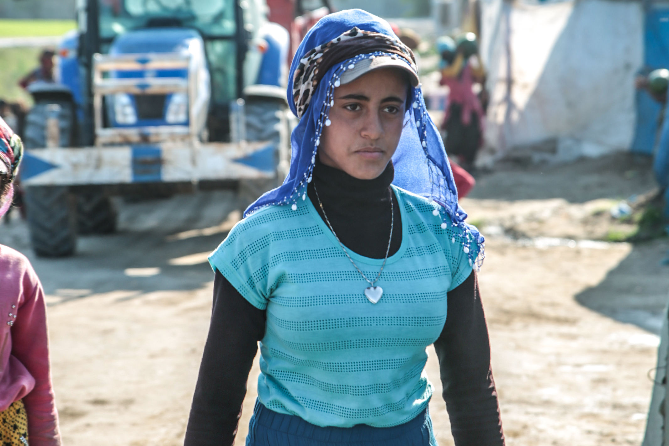 A Middle Eastern women who is a refugee in Greece walking through a camp wearing a head covering