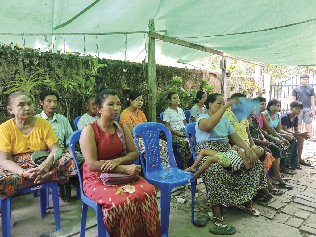 Christians in Cambodia sitting under a small pavilion in rows of blue lawn chairs for church