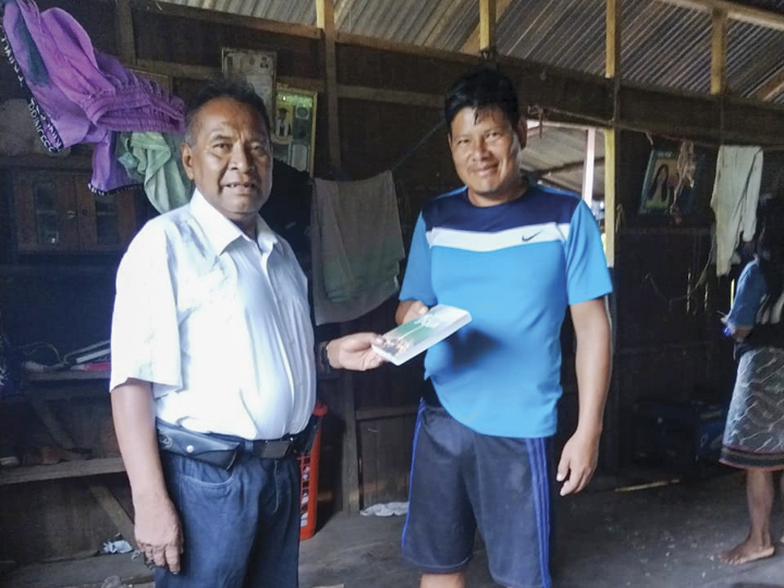 Christian missionary in Peru handing a Bible to a Peruvian man in a building with a tin roof