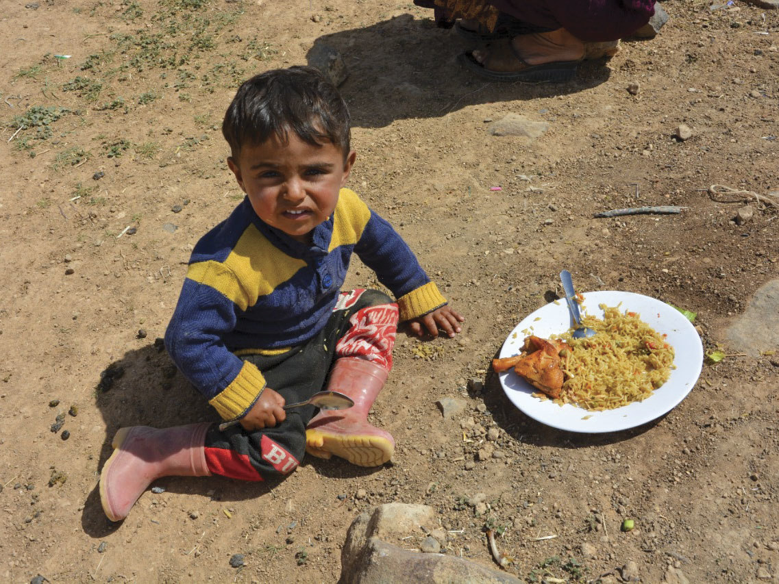 Refugee boy in Jordan eating while sitting on dirty ground in a refugee camp