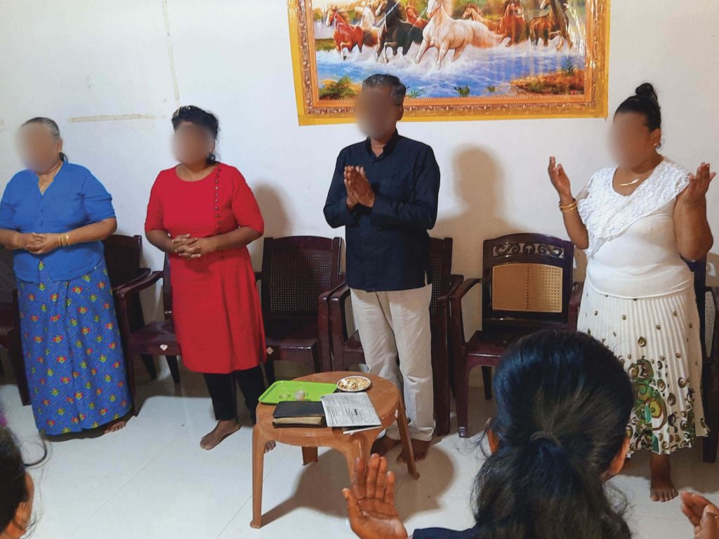 Christians in Sri Lanka standing indoors with their hands raised or folded while praying