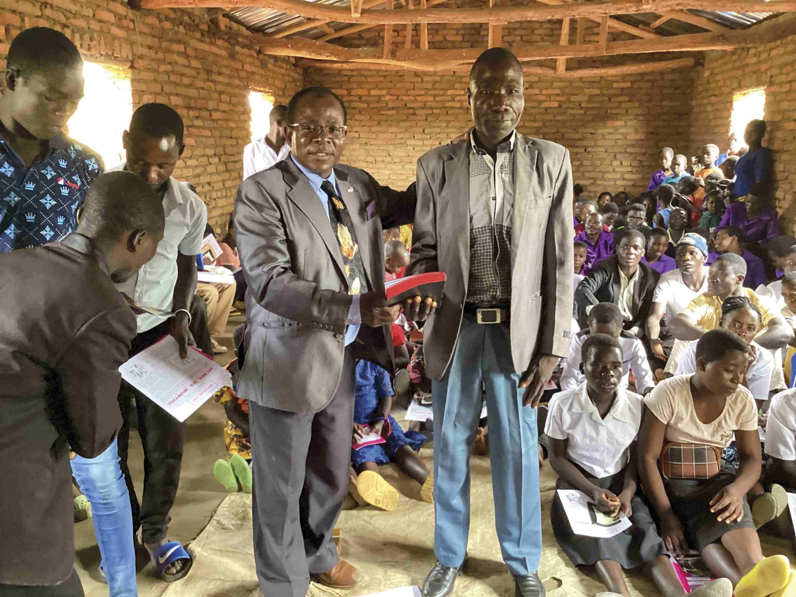 A Christian pastor in Malawi handing a Bible to a member of his church while in their church building