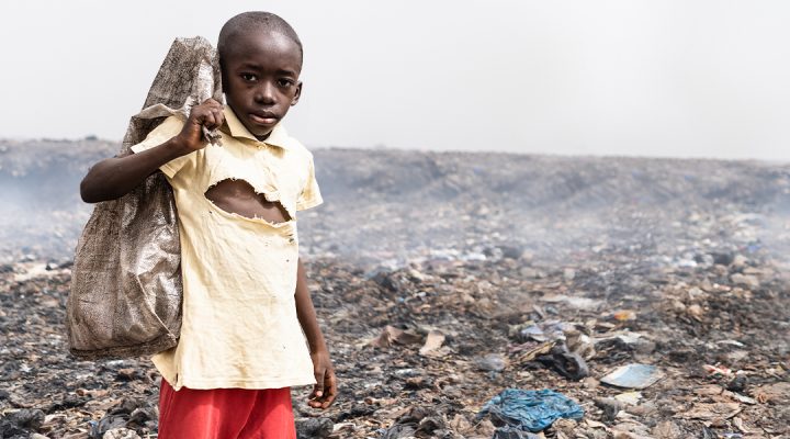 Young African boy standing in a landfill holding a burlap bag