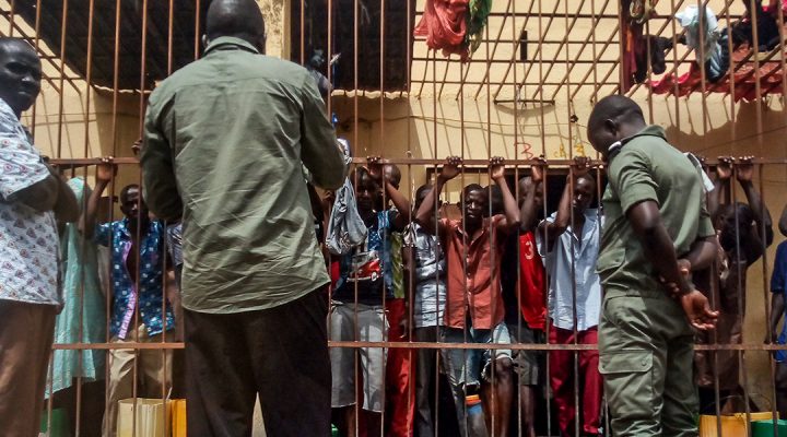 Jail inmates in Mali stand with their hands gripping the metal bars of their cell while a Christian missionary stands on the other side preaching the gospel